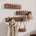 Three vertical wooden coat racks holding umbrellas, coats, and bags in sunlight
