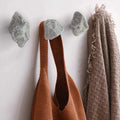 Stone wall hooks holding rust-orange tote bag and beige fringed scarf