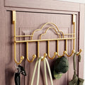 Gold over door hook rack on wood door with 7 hooks and cloud design holding cap bag and umbrella