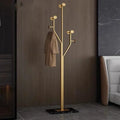 Gold arborescent coat rack with black marble base beside upholstered bed