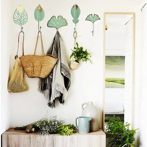 Mint green and gold leaf wall hooks displaying baskets blankets and plants on white wall